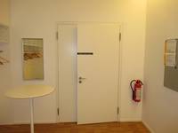 weiße Tür in weißer Wand, links von der Tür ein Spiegel und ein Stehtisch, rechts eine Wandtafel