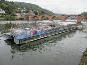 am Neckarufer asphaltierter Weg mit Stahlgeländer, Ponton und Anlegestelle mit Solarschiff, flacher Edelstahl-Kartamaran
