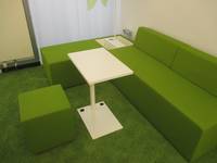 weißer kleiner Tisch mit einer grünen Bank und einem grünen Stoffhocker, grüner Teppichboden