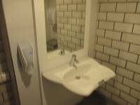 Waschbecken mit Spiegel, links Seifenspender an der Wand, rechts eine Wand