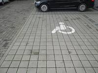 Ein Behindertenparkplatz mit quadratischen Betonpflastersteinen, als Bodenmarkierung ist ein großes Rollstuhlsymbol aufgemalt
