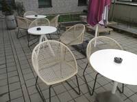 Eine gepflasterte Fläche im Freien mit runde Tischen und mehreren Stühle.
