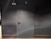 dunkle Tür, darüber ein Rollstuhlsymbol, Wand darum herum ist grau
