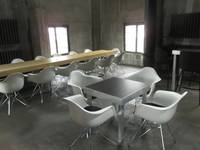 Raum mit Betonwänden und Fenstern, im Raum ein langer Tisch und ein kleiner Tisch, beide sind mit weißen Sesselstühlen umgeben