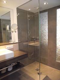 freihängender Waschtisch mit großem Spiegel links, rechts ebenerdig begehbare Dusche mit gläserner Kabine