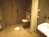 Eine Dusche mit einem Duschvorgang. An der dunklen Wand ist ein verschiebbarer Duschsitz angebracht.