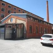Ehemaliges Fabrikgebäude aus Backstein mit Glasanbau, im Hof davor parkt ein weißes Auto