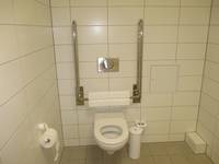 Eine weiße Toilette mit Haltegriffen rechts und links an einer weiß gekachelten Wand