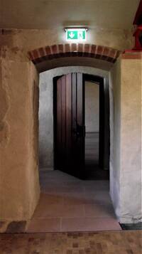 offener Durchgang mit bogenförmigen, gemauerten Türsturz, danach nach innen aufstehende massive Holztür mit schmiedeeisernem Griff