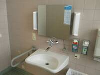 Weißes Waschbecken mit Spiegel und Seifenspender. Links vom Waschbecken ist ein Haltegriff
