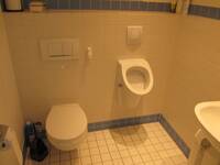 Eine Toilette und ein Pissoir an einer hell gekachelten Wand