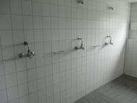 Ein Raum mit einer weiß gefliesten Wand und mehreren Duschplätzen
