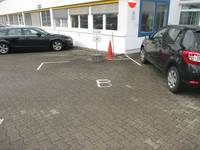Behindertenparkplatz mit Bodenmarkierung und Schild, links und rechts daneben parkende Autos