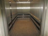 geöffneter, sehr geräumiger Aufzug mit metallverkleideten Wänden, einem Handlauf rechts und dem Bedienelement links 