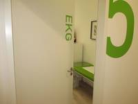 offenstehende einflügelige weiße Tür in einer weißen Wand, auf der Tür ist ein grüner Schriftzug  EKG