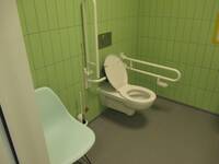 Eine weiße Toilette an einer hellgrün gekachelten Wand mit je einem Haltegriff auf jeder Seite.