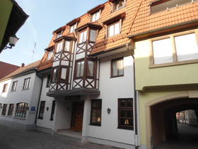 weiße Häuserzeile. 3 Stockwerke mit Gaubenfenstern im braunen Dach. Bildmitte Eingang ins Hotel, daneben rechts Durchfahrt in den Innenhof.