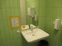 Ein weißes Waschbecken an einer grünen Wand. Über dem Waschbecken ist eine Spiegel.