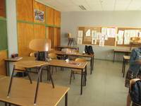Klassenzimmer mit Tischen und Stühle, im Hintergrund links ein deckenhoher Einbauschrank aus hellem Holz