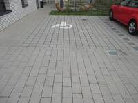Ein Parkplatz aus Betonverbundsteinen mit einem großen, aufgemalten Rollstuhlsymbol als Bodenmarkierung.