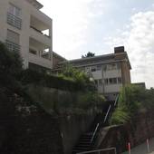 mehrstöckiges Schulgebäude mit Flachdach an einem Hang, mehrere Treppen führen nach oben,der Hnag ist teilweise bewachsen