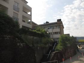 mehrstöckiges Schulgebäude mit Flachdach an einem Hang, mehrere Treppen führen nach oben,der Hnag ist teilweise bewachsen