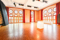 Ein Raum mit einer Fensterfront mit verzierten Fenstern, an der Decke hängt Bühnenbeleuchtung