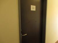 Eine dunkle Tür in einer hellen Wand. Auf der Tür ist ein Schild mit der Nummer 228 angebracht.