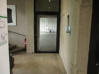 einflügelige Glaseingangstür mit Oberlicht, in einem dunklem Rahmen. Vor der Tür ein Flur, links Treppenansatz, rechts Betonwand 