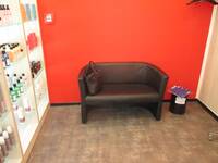 Ein dunkles Sofa vor einer roten Wand, links Regale mit Haarpflegeartikeln