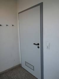 weiße Tür in einer weißen Wand, die Tür hat einen grauen Rahmen und einen schwarzen Türgriff