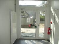 Eine Glastür mit einem weißen Rahmen, rechts hängt ein roter Feuerlöscher an der Wand.