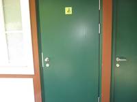 grüne Tür in einem braunen Rahmen,  darauf ein gleber Aufkleber mit Rollstuhlsymbol