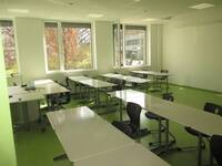 Klassenzimmer mit Tischen, Stühlen und offenstehenden Fenstern