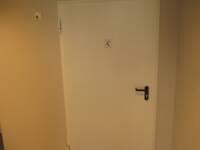 Eine weiße Türe in einer hellen Wand. Auf der Türe ist ein Rollstuhlfahrersymbol