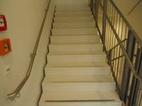 Treppe mit einem Handlauf links und rechts, jede Stufe ist mit einem Streifen markiert