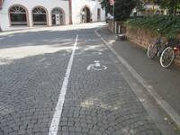 2 längs auf dem Kopfsteinpflaster-Straßenbelag eingezeichnete Behhindertenparkplätze mit Rollstuhlsymbol als Bodenmarkierung