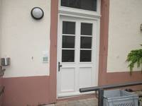 weiße Tür mit Sprossenfenster und Sandsteinrahmen. Links daneben runde Außenleuchte
