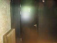 schwarze Tür in einer schwarzen Wand. Auf der Tür ist Rollstuhlsymbol. Links Betonwand mit einem Heizkörper